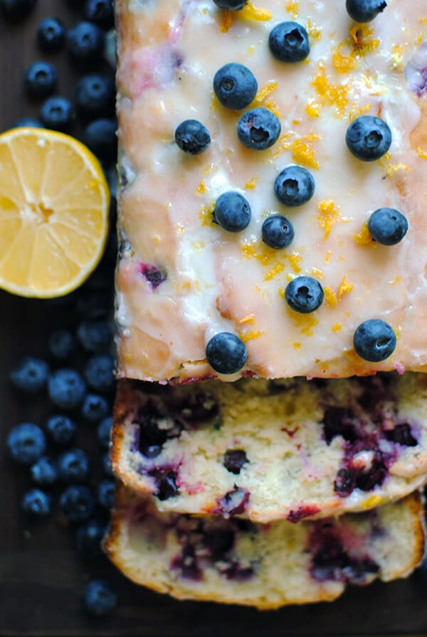 Lemon Blueberry Bread on a cutting board with fresh blueberries